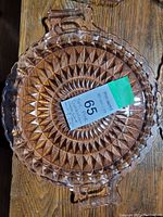Round pink Depression glass bowl with scalloped edges and diamond pattern on wooden surface including auction label