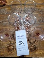 Seven pink Depression glass wine glasses arranged on wooden surface with a MaxSold lot card.