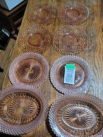 Overview of eight pink Depression glass pieces on wooden table, showing plates and serving dishes with detailed pressed glass patterns.