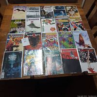 Overview photo showing full assortment of 20 comics laid out in 4 rows of 5 comics each, some in plastic sleeves, on a brown wooden surface.