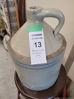 Front and side view of large ceramic jug with blue lines and sturdy handle.