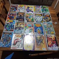 Wide shot showing 20+ assorted superhero comics spread on table, featuring Spiderman, Superman, Batman, Justice League and more.