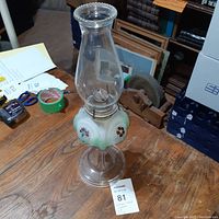 Side view of green glass oil lamp showing the floral design on the base, glass chimney, and metal burner.