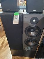 Photo of two large Kenwood speakers side by side, one with the front grille removed showing three drivers and a tweeter and the other with the grille on.