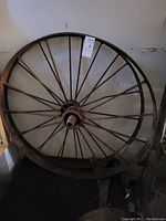 Front view of one vintage metal wagon wheel, showing spokes and rusted metal rim.