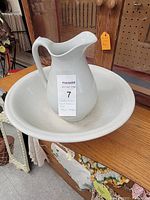 Photo of white ceramic pitcher sitting inside matching basin on wooden table, showing overall condition and size.