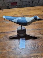 Side view of the wooden warble bird decoy with painted black, gray, and white details on a wooden base.
