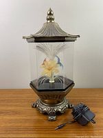 Full view of the 1970s pagoda fibre optic lamp showing the metal pagoda roof, clear panels, floral fiber optic light inside, ornate base, and attached power cord.