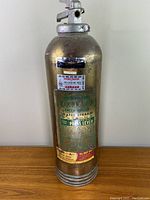 Full view of the antique fire extinguisher showing its gold/brass finish and metal top with press lever.