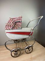 Side view of antique Lloyd Carriage baby doll stroller showing red and white striped canopy and metal frame with wheels.