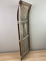 Side view of the antique wood sled showing curved structure, wooden slats, and metal side supports.