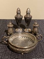 Photo showing full set including silver dish with glass bottom and three pairs of silver salt and pepper shakers arranged behind it.