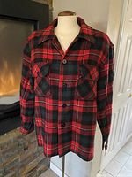 Front view of a red, black, and green plaid wool blend flannel jacket on a mannequin, showing button-down front and chest pockets.