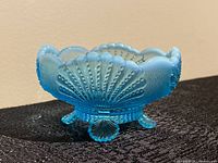 Side angle view of the blue opalescent scalloped shell candy dish with textured shell design and three shell-shaped feet.