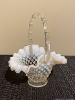 Front angled view of small vintage Fenton hobnail glass basket showing ruffled opalescent white edge and clear textured handle.