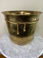 Front and full view of the hammered brass planter sitting on marble surface.