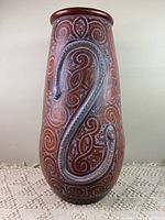 Full front view of the terracotta vase showing one side of the double-headed snake design and geometric patterns with swirl and maze-like carvings.