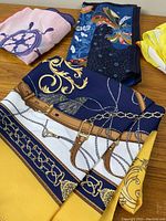 Four folded vintage printed handbag scarves arranged on wooden surface showing partial designs including nautical and mid century modern themes