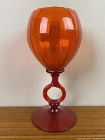 Front view of bright orange art glass snifter showing the rounded faceted bowl and keyhole stem on a broad base.