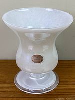 Front view of white Murano art glass vase showing flared top, bulbous body and round pedestal base with Murano label attached on body.