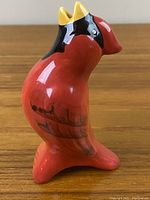 Front-right side view of glossy ceramic cardinal figurine showing red body, yellow and black head details, and painted wings.