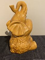 Front view of vintage ceramic elephant statue, showing detailed facial features, ears, trunk raised upwards, and embossed decorative patterns on the body.