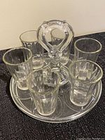 Glass drink caddy with six ribbed glass cups arranged on a black surface, showing caddy design and cup style.