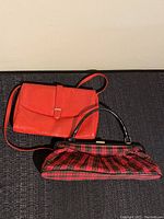 Both vintage handbags displayed side by side: red textured purse and Le Chateau plaid handbag with black rounded handles and brass clasp.