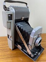 Front angled view showing extended folding bellows, lens, and carrying strap.