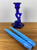 Cobalt blue glass koi fish shaped candle holder with two light blue twist spiral taper candles placed in front on wooden surface
