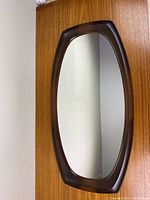 Photo of vintage Syroco 1970s vanity mirror showing oblong retro shape and dark brown plastic frame against a wooden door.