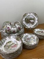 Complete 41 piece vintage Johnson Bros dinnerware set arranged on table with variety of plates, bowls, and cups decorated with English winter village scenes and decorative borders