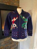 Front view of a blue wool knit sweater showcasing a colorful ice skating couple design with full zip closure, ribbed collar, cuffs, and hem.