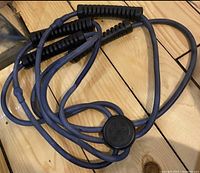 Photo of four navy blue resistance exercise bands with black foam handles connected to a central circular piece on wooden floor.