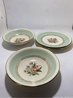 Two bowls and three plates shown stacked with floral pattern and mint green border with gold accents