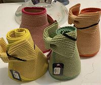 Rolled up green woven sun hat, showing flexible structure and adjustable strap, alongside other colored hats for visual reference.
