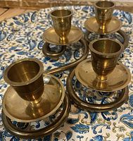 Photo showing a vintage brass candle holder with four tapered candle holders connected in a circular design placed on a patterned surface.