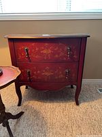 Front view of the red two-drawer chest with gold floral embellishments and metal handles, showing chipped area on front.