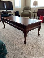 Side view of the solid wood coffee table showing the two drawers and cabriole legs on carpeted floor.