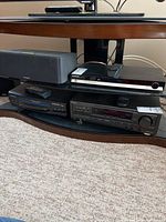 Samsung DVD-HD860 DVD player along with Panasonic VHS player on shelf with remotes revealed on top of devices.