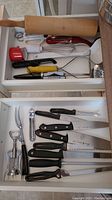 Two kitchen drawers showing various kitchen utensils including rolling pin, whisk, measuring cup, and multiple knives.