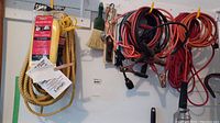 Photo showing two extension cords, booster cable, ropes, and lighters hanging on hooks.