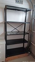 Full view of black metal shelving rack with four shelves and cross brace at back.