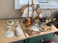 Photo showing two miniature wooden ship models, figurines, shell plaques and other decor items on dresser