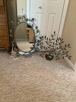 Photo showing the oval metal framed mirror positioned beside the metal leaf and branch wall decor on the floor.
