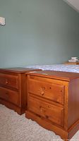 Side-by-side view of both matching wooden night stands next to a bed against a green wall.