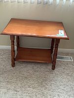 Front view of the solid wood occasional table showing rectangular top, turned legs, and lower shelf.