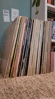 Side view of approximately 30 vinyl records standing vertically showing the variety and thickness of the collection.