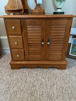 Front view of Roxton maple cabinet showing three small drawers on left, two louvered cupboard doors on right, white knob handles, and scalloped base.