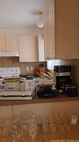 Photo shows countertop with Crock-Pot slow cooker, 2-slice toaster, Dazey waffle maker, hand mixer, black carving set case, and several glassware items below.